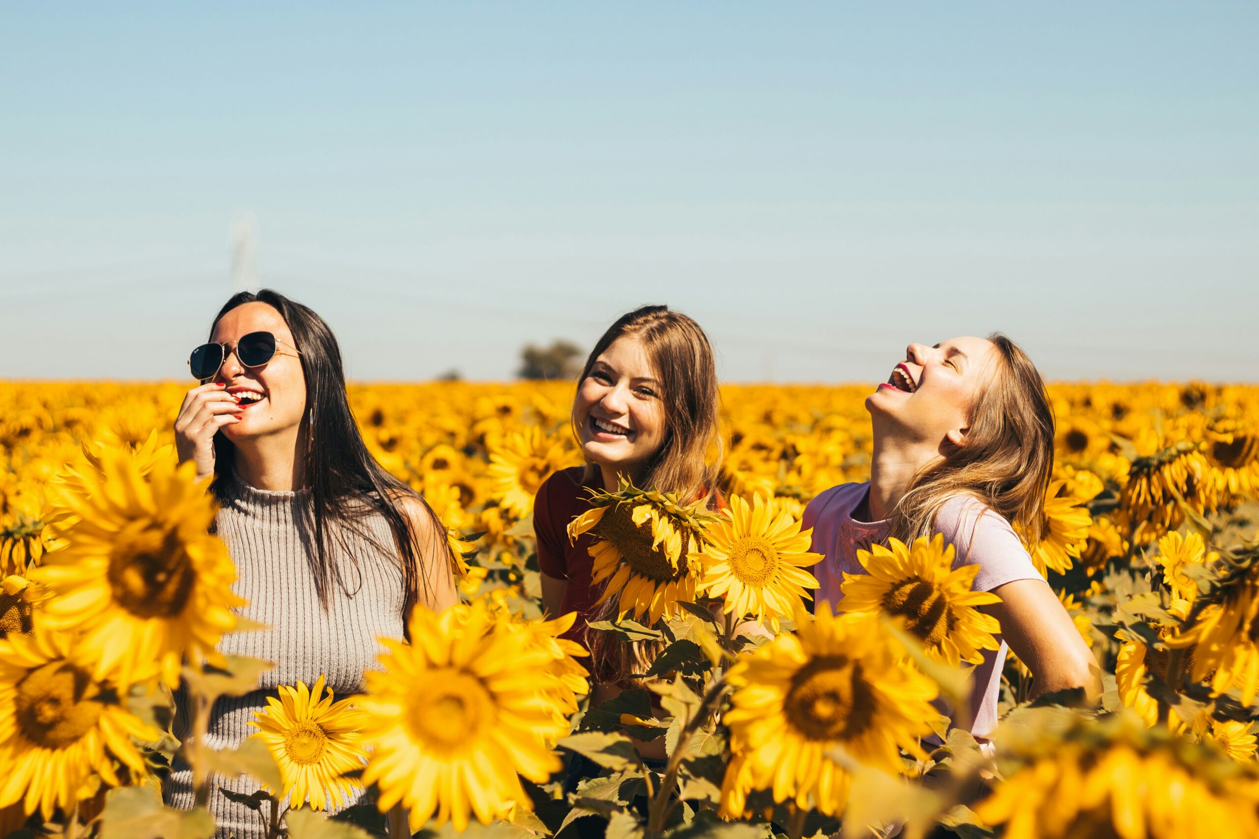 girls laughing in a field of sunflowers | hiddenriverhealing.com