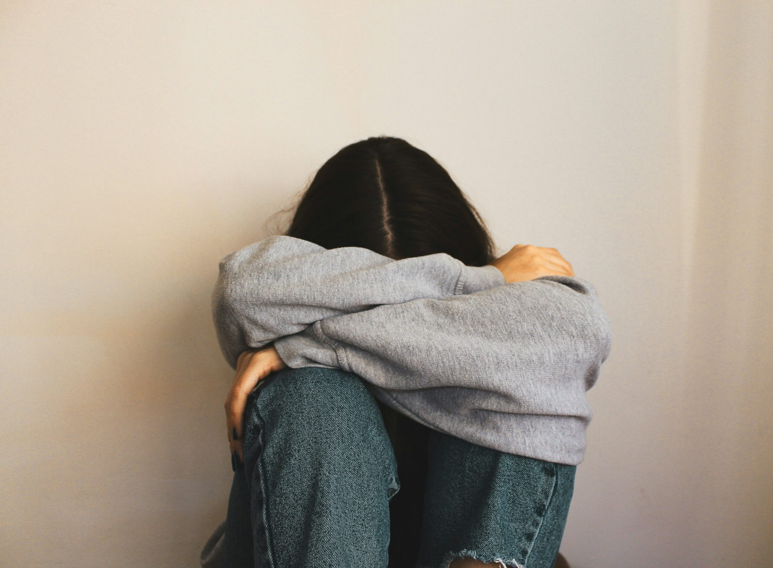 girl wearing a gray sweatshirt sitting alone with her head down | hiddenriverhealing.com