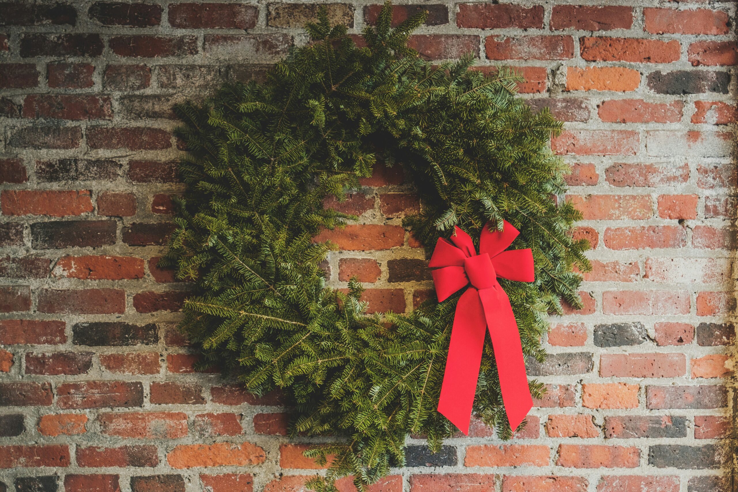 holiday wreath with red bow on brick wall | hiddenriverhealing.com